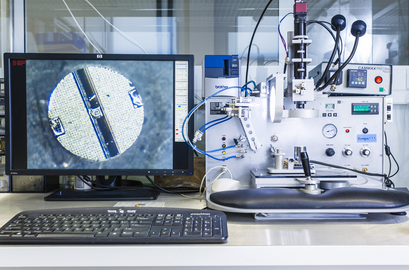 widok na monitora komputera, na kt&oacute;rym widać zbliżenie na kolisty komponent elektroniczny. Obok monitora znajduje się specjalistyczna aparatura z diodami i pokrętłami