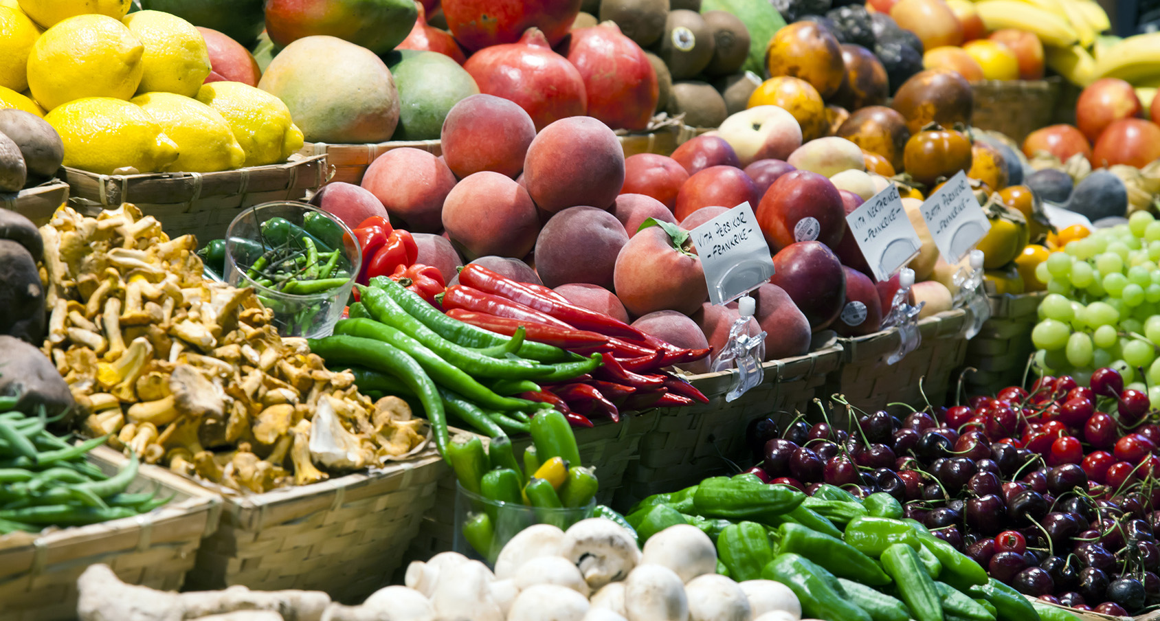 widok na stragan z warzywami i owocami, widać m.in. zielone papryki pieczarki oraz czerwone jabłka