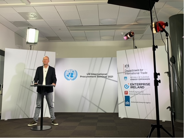 Łysy mężczyzna w średnim wieku, w okularach, stoi przy m&oacute;wnicy w pustej sali