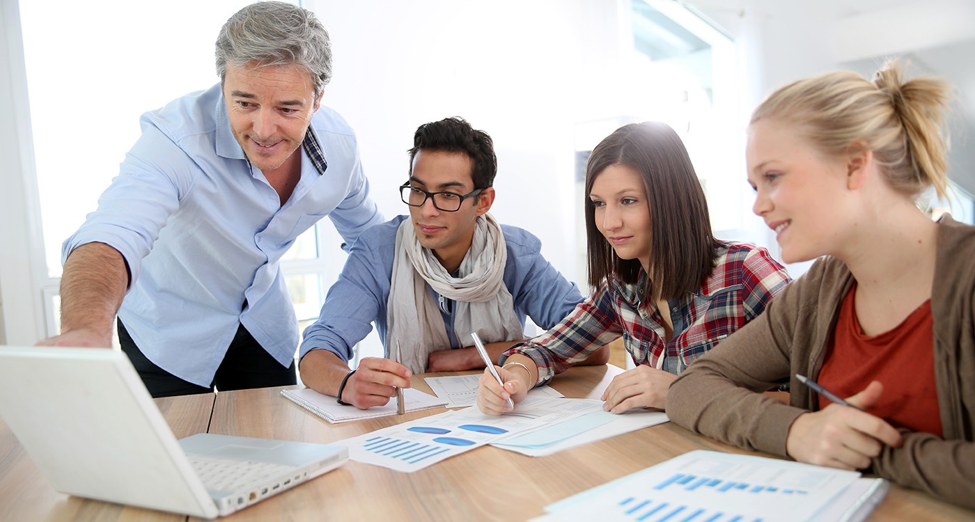 Grupa ludzi siedzi przy biurku i patrzy się w monitor