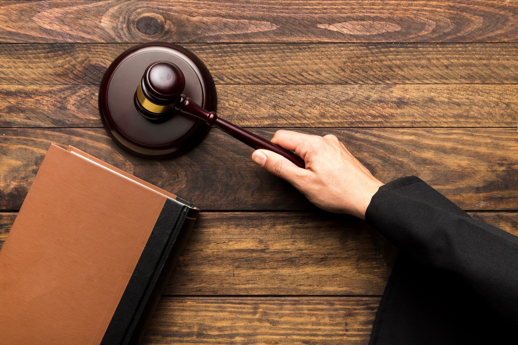 widok z g&oacute;ry na st&oacute;ł sędziego. Widać jego rękę trzymającą młotek i uderzając w drewnianą kołatkę, postawioną na biurku