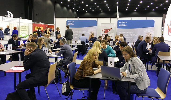 Sala ze stolikami, przy kt&oacute;rych siedzą ludzie i rozmawiają ze sobą