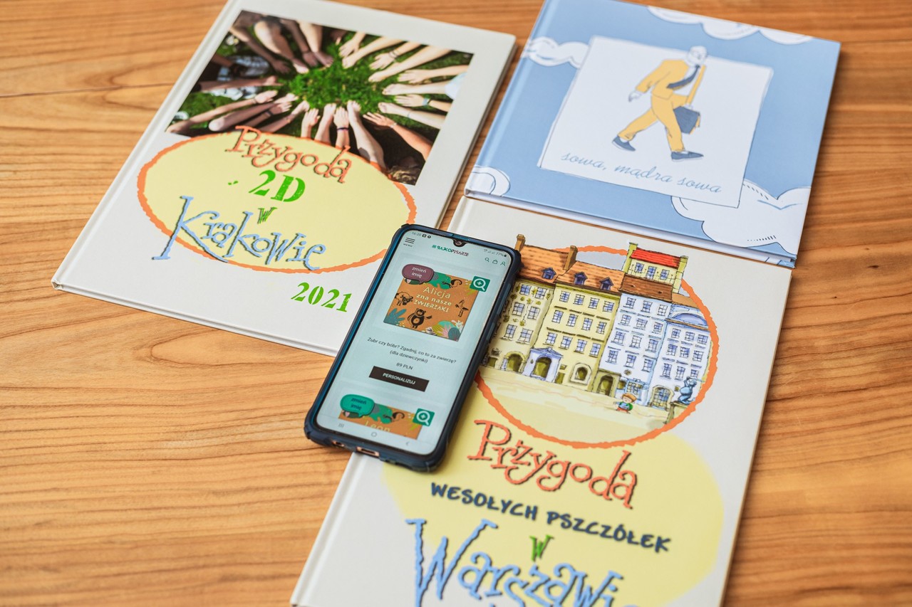 Trzy katalogi leżą na blocie, na nich telefon kom&oacute;rkowy