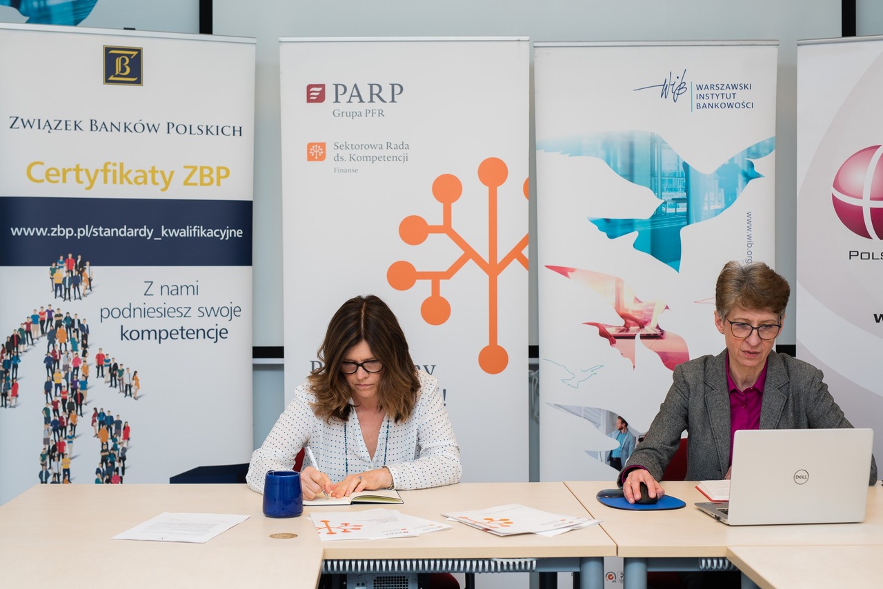 Dwie kobiety siedzą na tle rollup&oacute;w