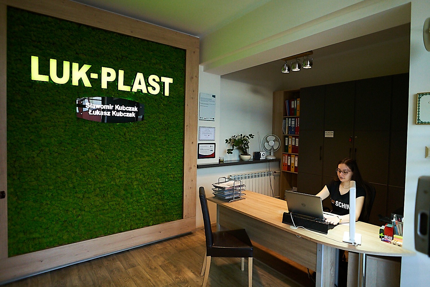 wnętrze biura firmy Luk plast przy biurku siedzi kobieta w okularach i pisze na komputerze 