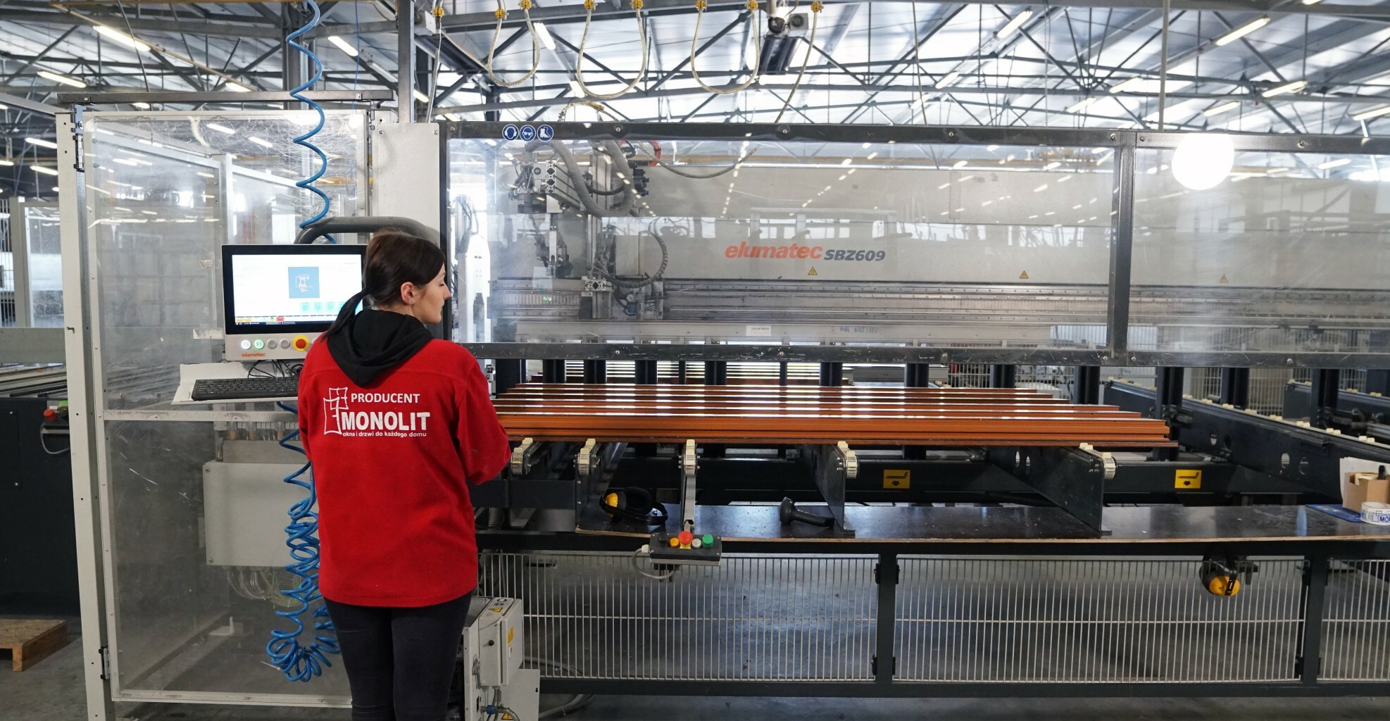 hala fabryczna przy maszynie pracownik odkręcony tyłem do obiektywu aparatu 